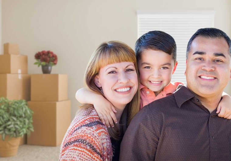 Photo of a smiling family in front of moving boxes in their house