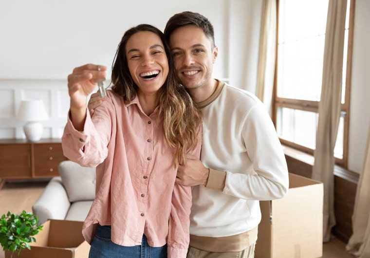 A photo of a couple smiling in a house with a key to their new home